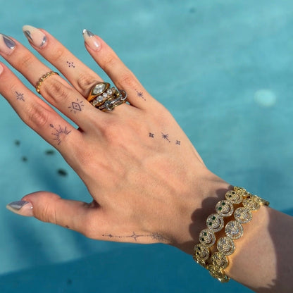 Hand with multiple rings and bracelets against a blue water background