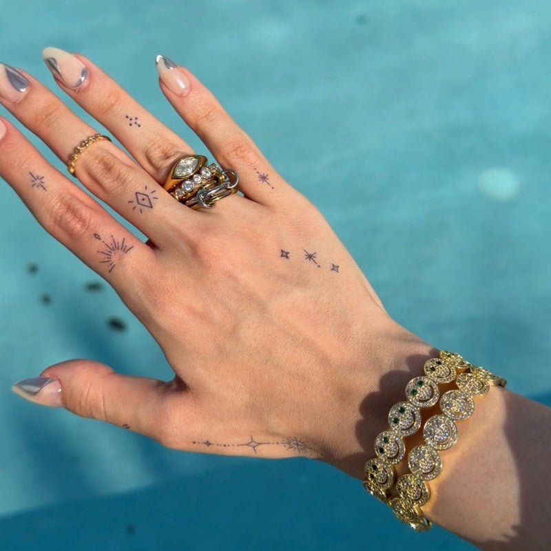 Hand with multiple rings and bracelets against a blue water background